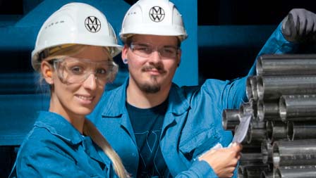 Photo of two employees in front of a stack of steel tubes